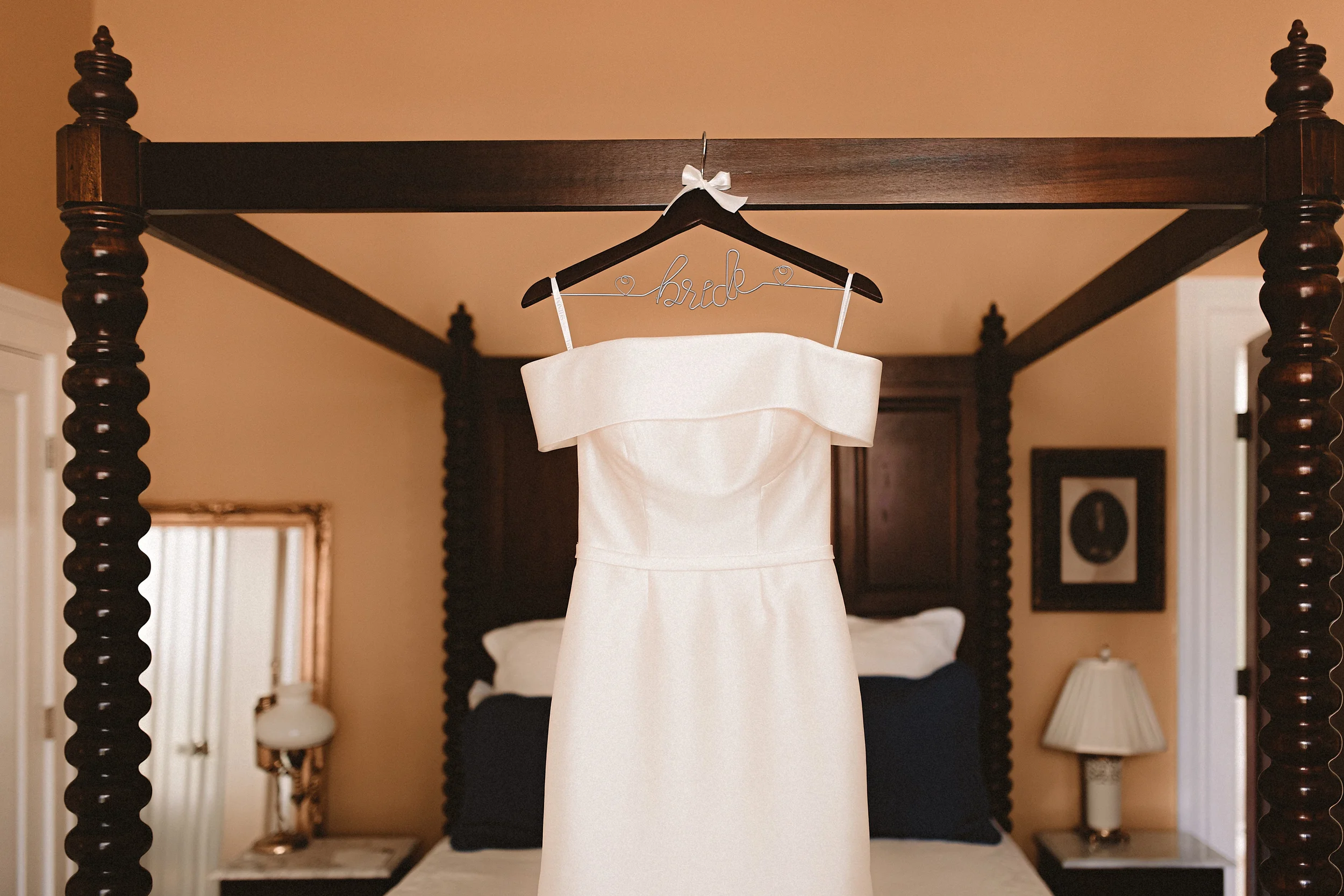 Bride's wedding dress hanging on a four-poster bed inside the historic Denny House bridal suite.